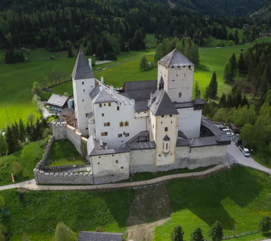Mittelalterliche Burg mit weißen Türmen inmitten grüner Hügel und Wald